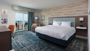 A hotel room with a large bed, a desk, a chair, a balcony with a view, and a wall with a patterned design. - Hampton Inn & Suites Manistee Waterfront (Manistee)