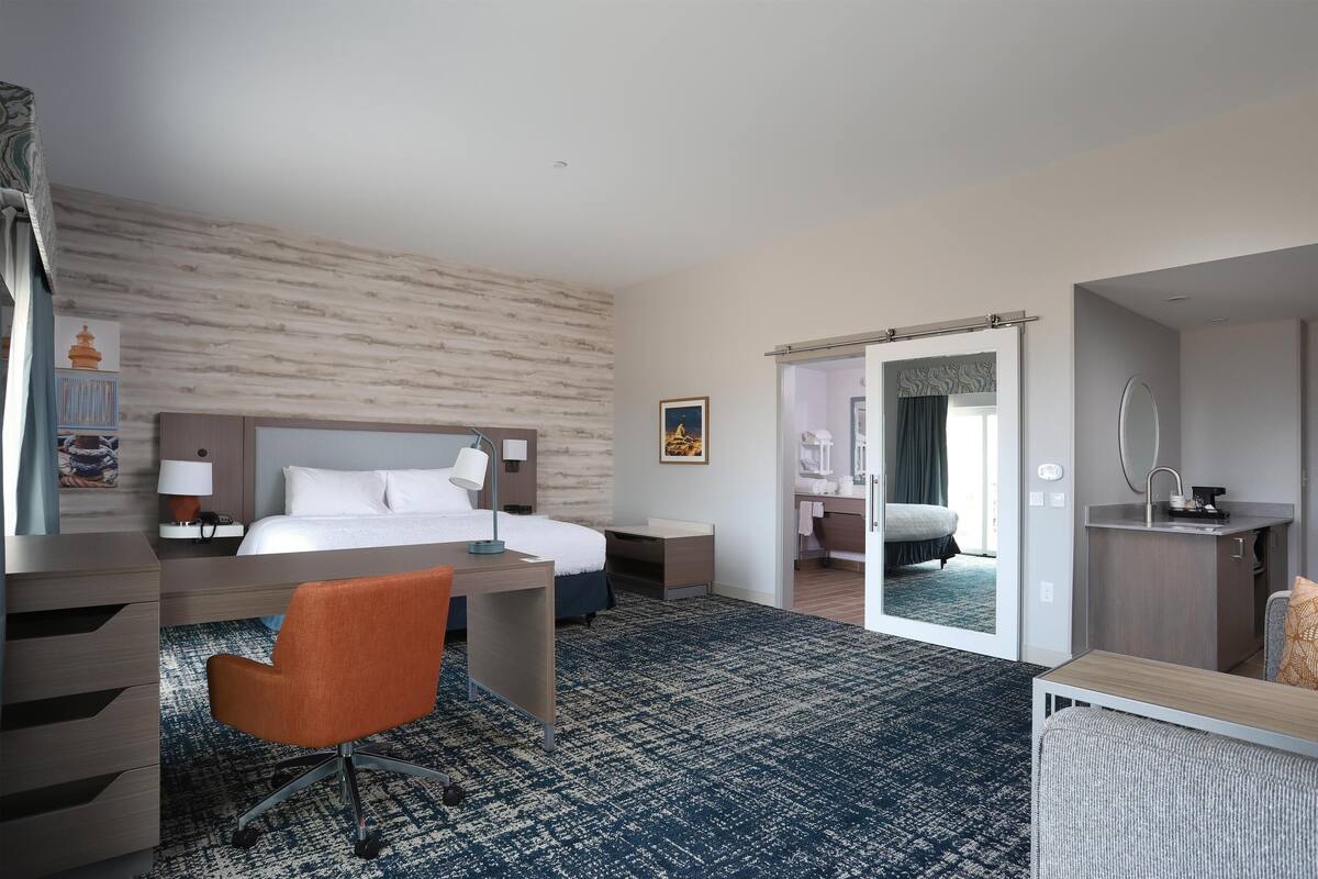 A hotel room with a bed, desk, chair, and a bathroom visible through an open door.