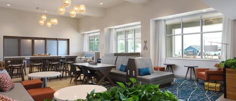A spacious living area with a sofa, coffee table, and dining table. There are multiple seating options and a large window providing natural light.