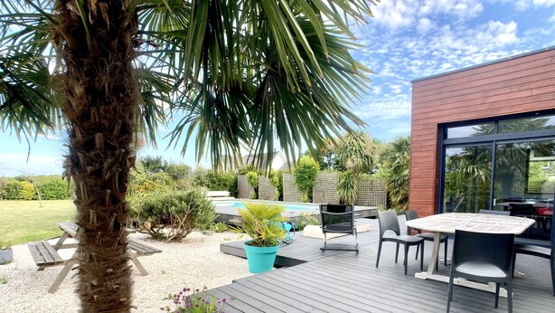 Een houten terras met buitenmeubilair, een zwembad en een tuin met diverse planten.