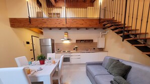 Cozinha moderna com teto de madeira, área de refeições com mesa e cadeiras, e um sofá cinza com manta.