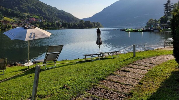Vista para o lago com área gramada, um banco e um guarda-sol.