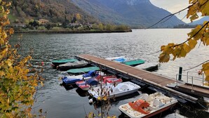 Um cais com vários barcos, um lago calmo e montanhas ao fundo.