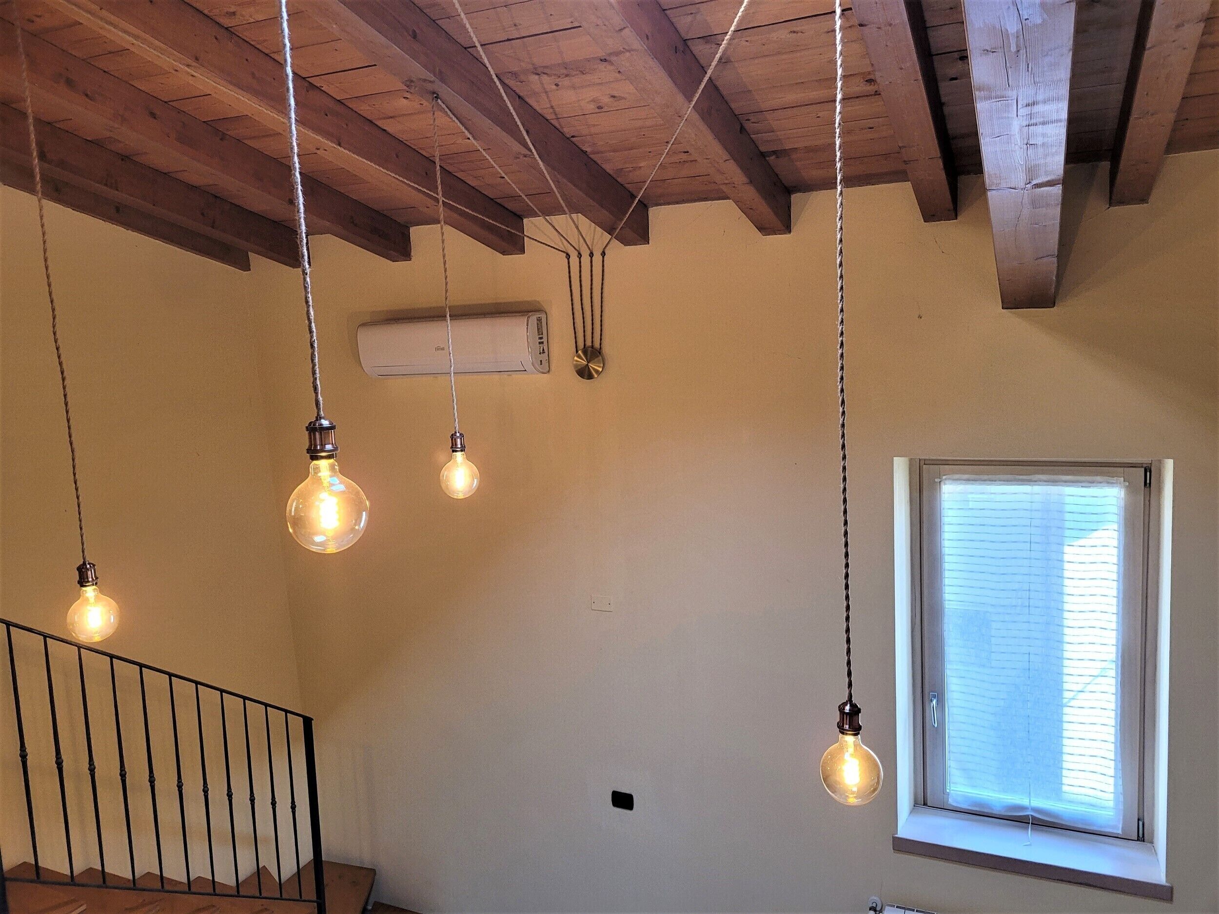 A room with exposed wooden beams, a staircase, and hanging light bulbs.