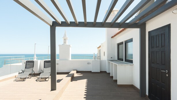 Un balcon avec deux chaises longues, une porte et une vue sur la mer.
