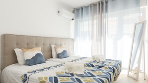 Un lit bien fait, avec une couvre-lit à motifs, une tête de lit et une table de chevet surmontée d’une lampe.