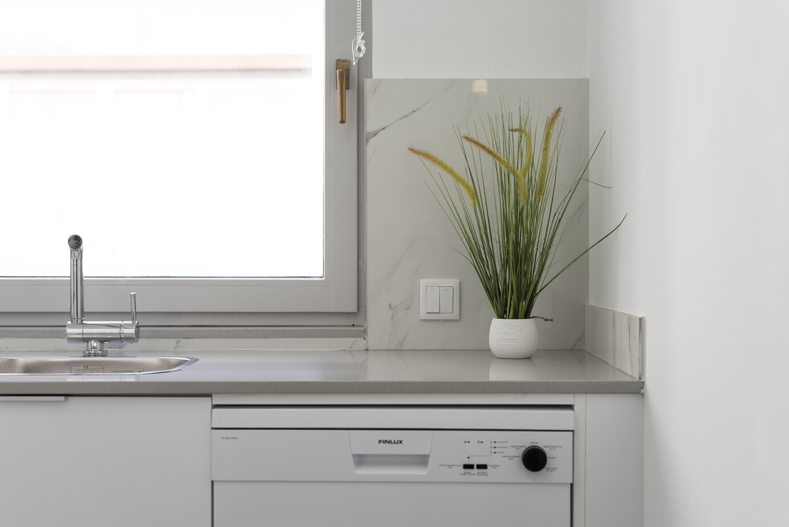 A modern kitchen with a built-in dishwasher, a window above the sink, and a potted plant on the countertop.