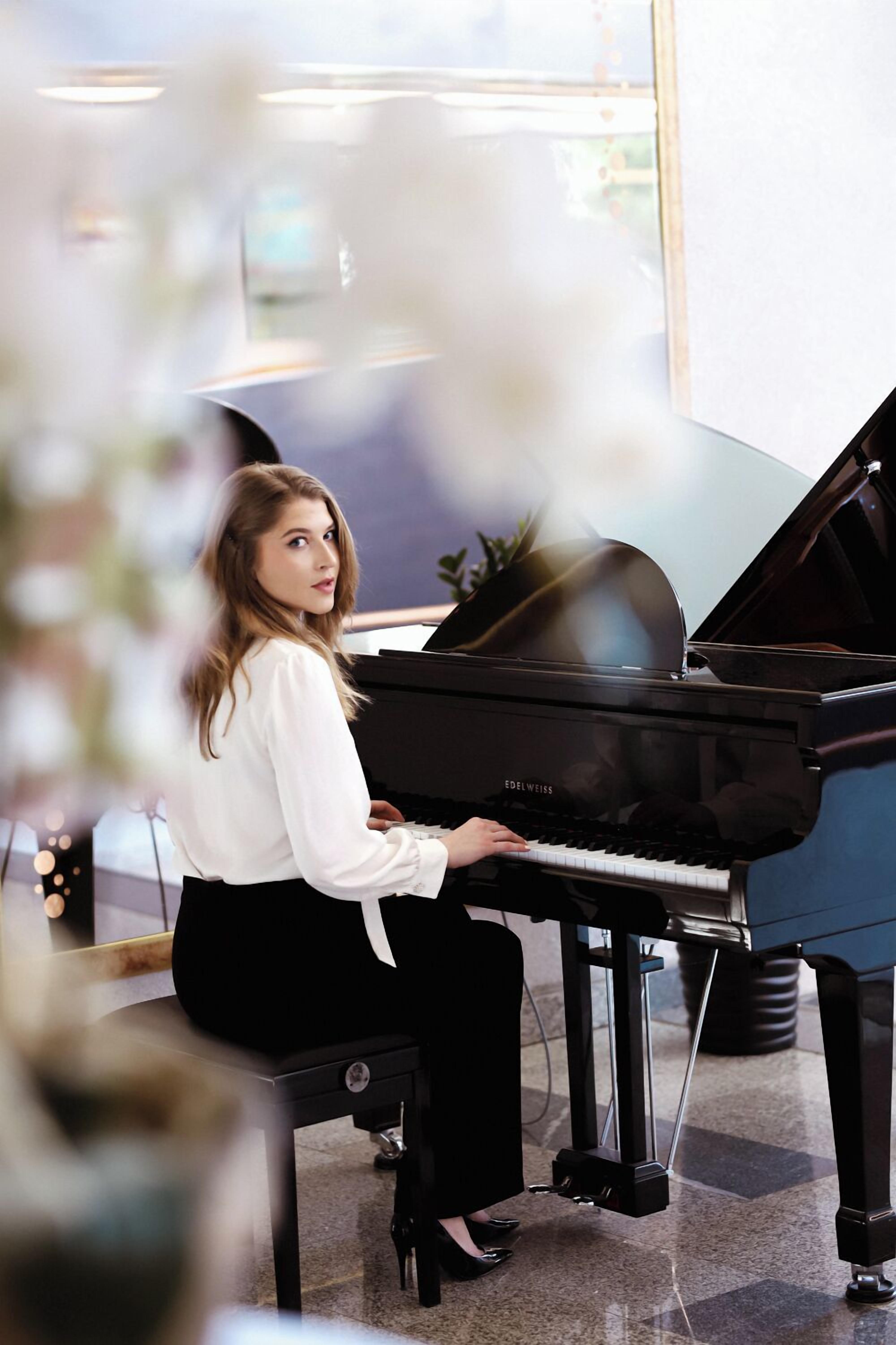 A person seated at a grand piano in a well-lit room with a modern design.