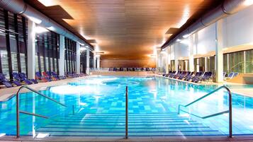 Una piscina interior con baldosas azules cristalinas, barandillas metálicas y filas de sillones de relax a lo largo de los bordes.