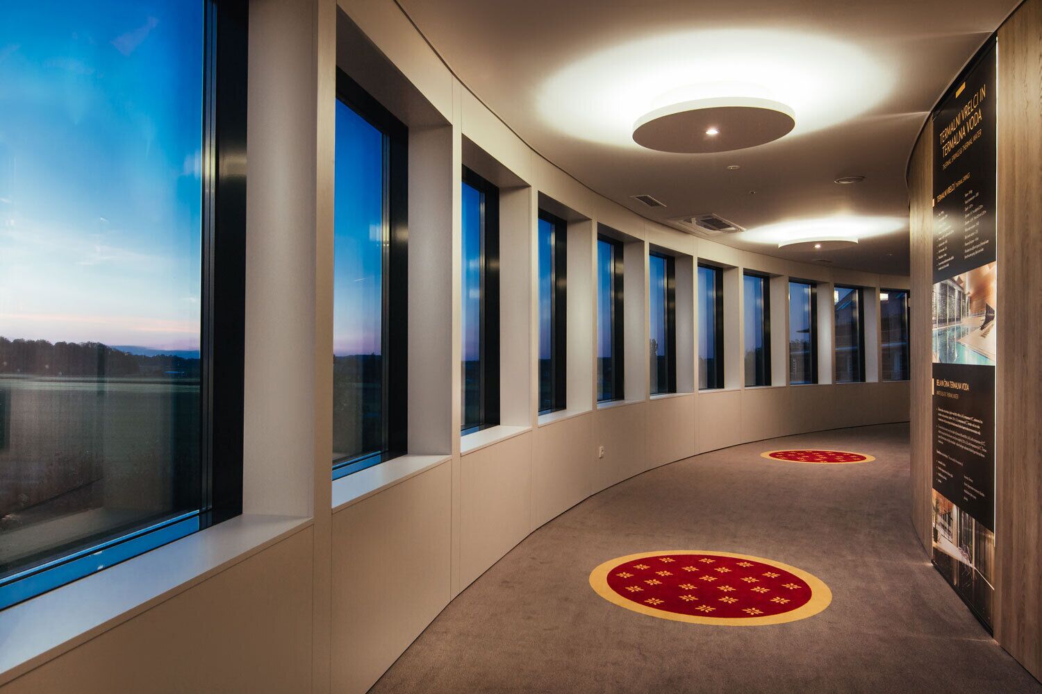 Un couloir doté de grandes fenêtres, d’un plafond incurvé et d’un sol recouvert de moquette orné d’un motif circulaire.