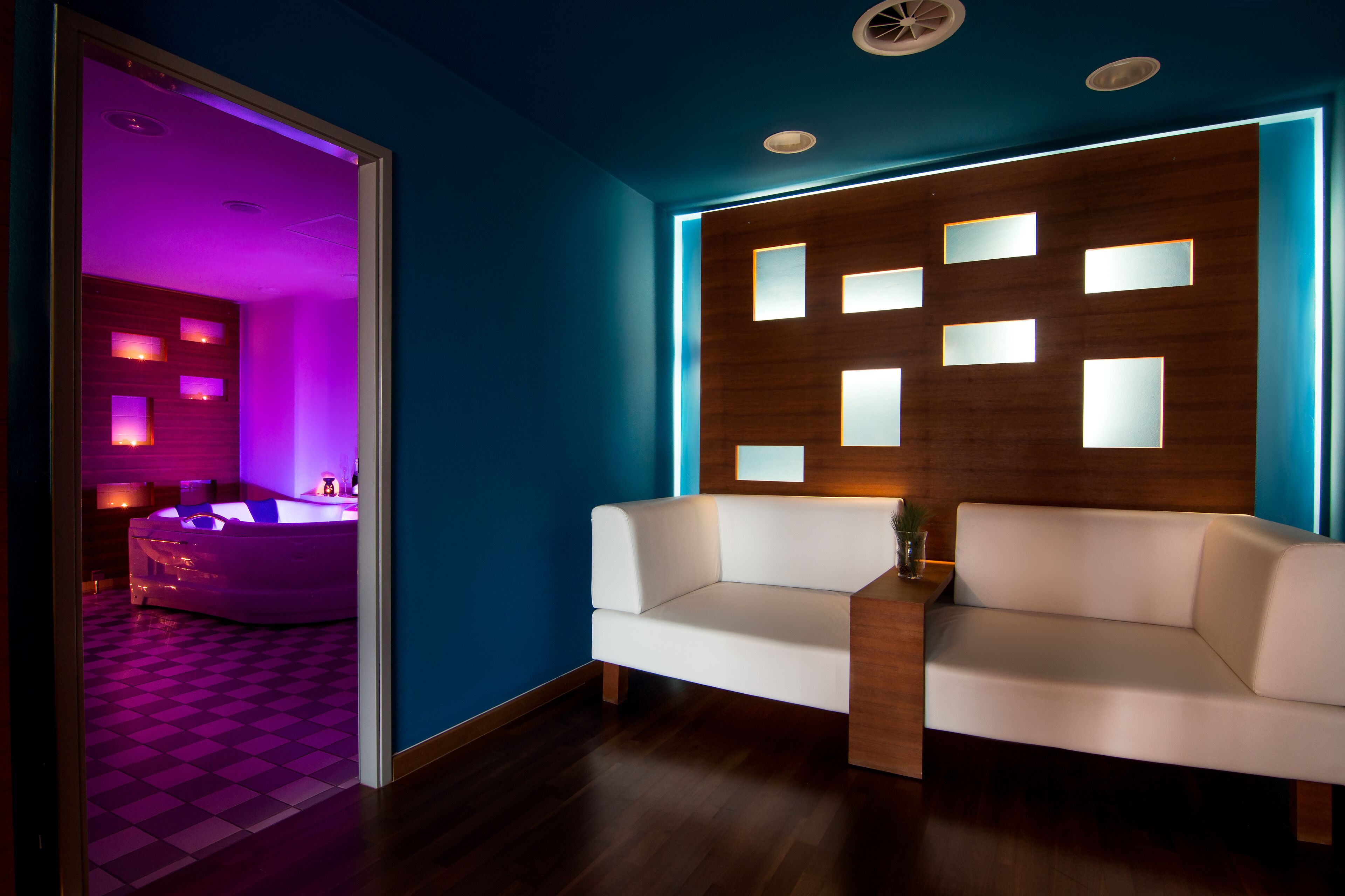 A modern room with a white sofa, a wooden accent wall with illuminated panels, and a checkered floor.