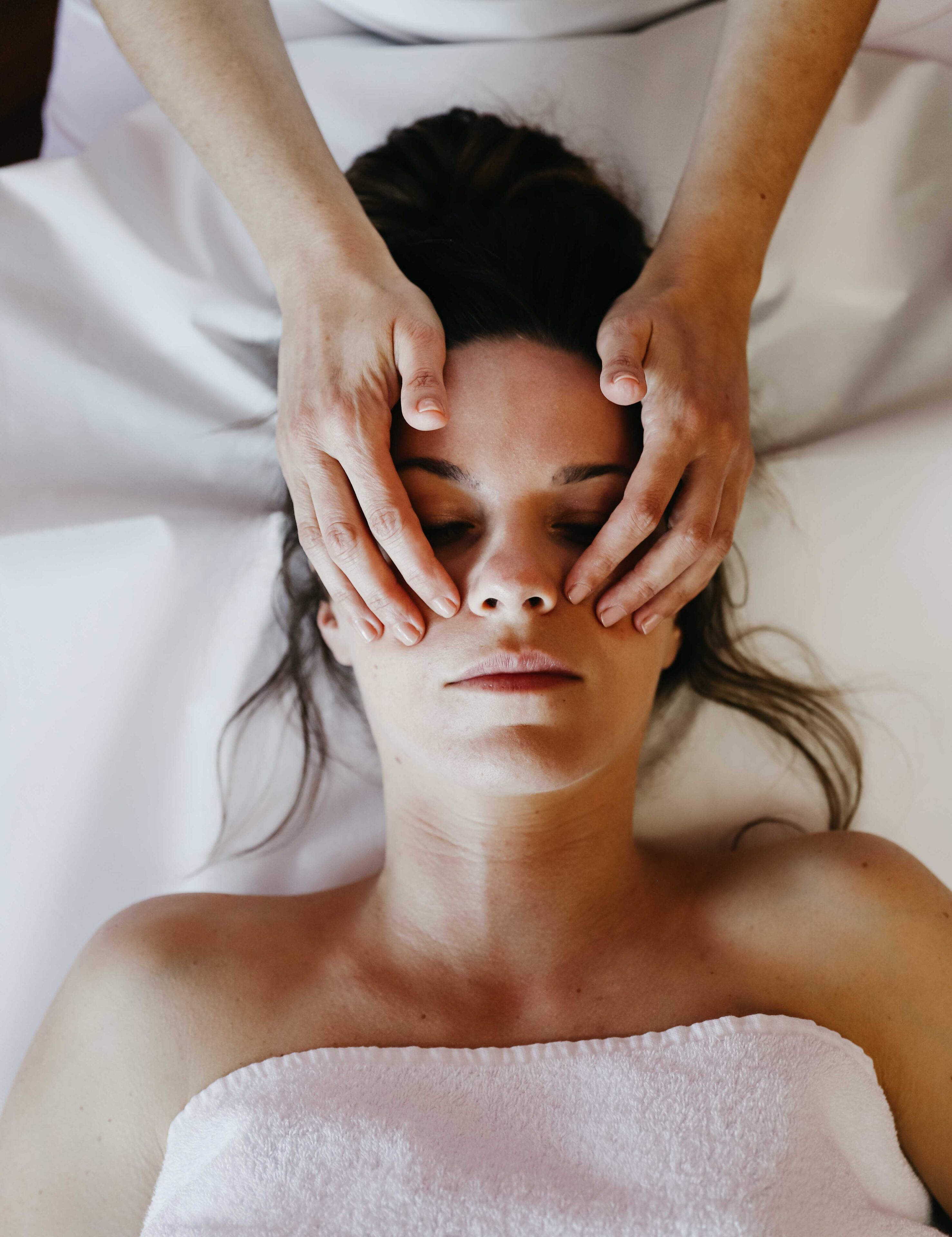 A person lying on a bed with a white towel wrapped around their shoulders.