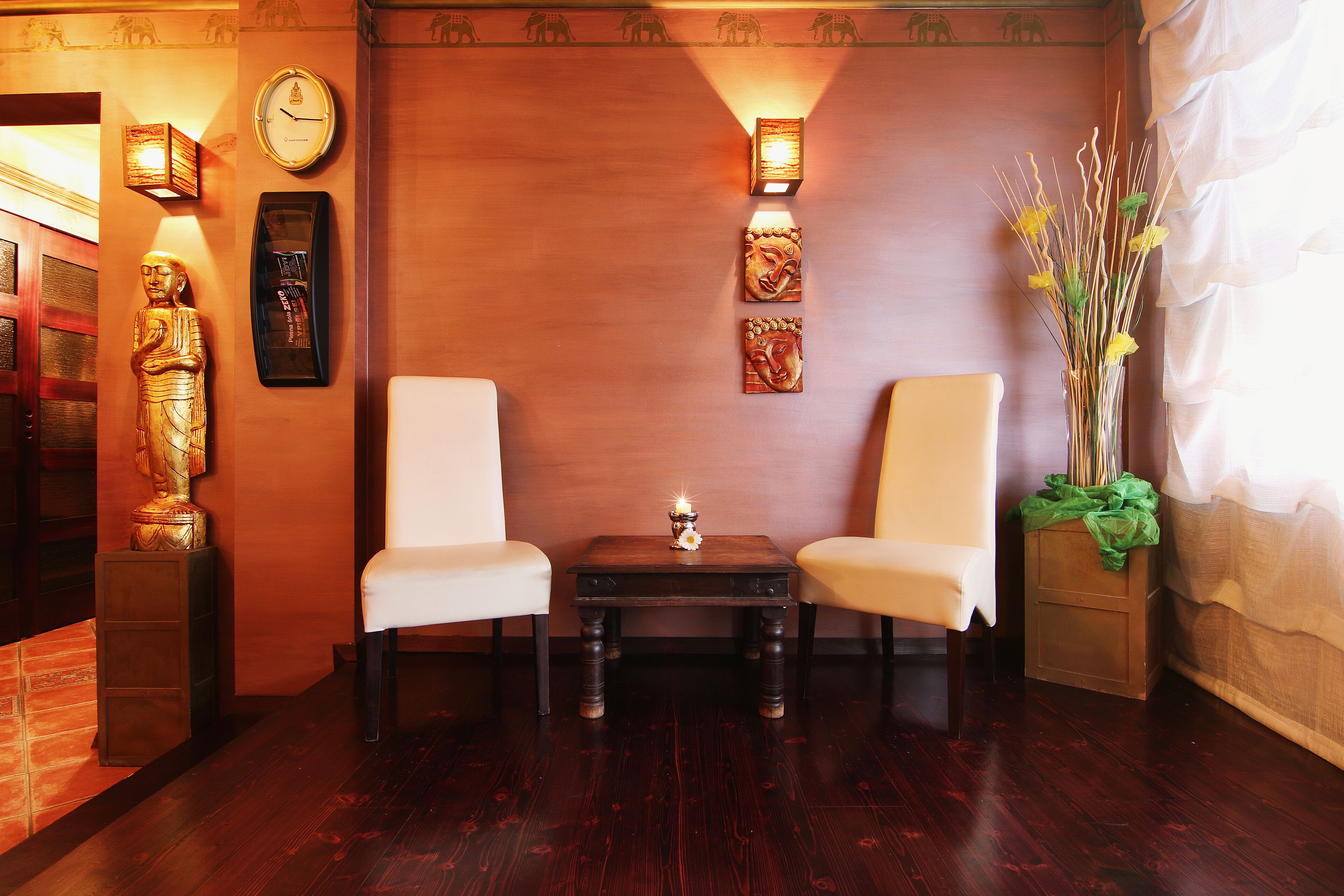 A room with two white chairs, a small table with a candle, and wall decorations including a clock and framed artwork.