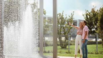 A couple standing by a fountain with a modern building in the background.