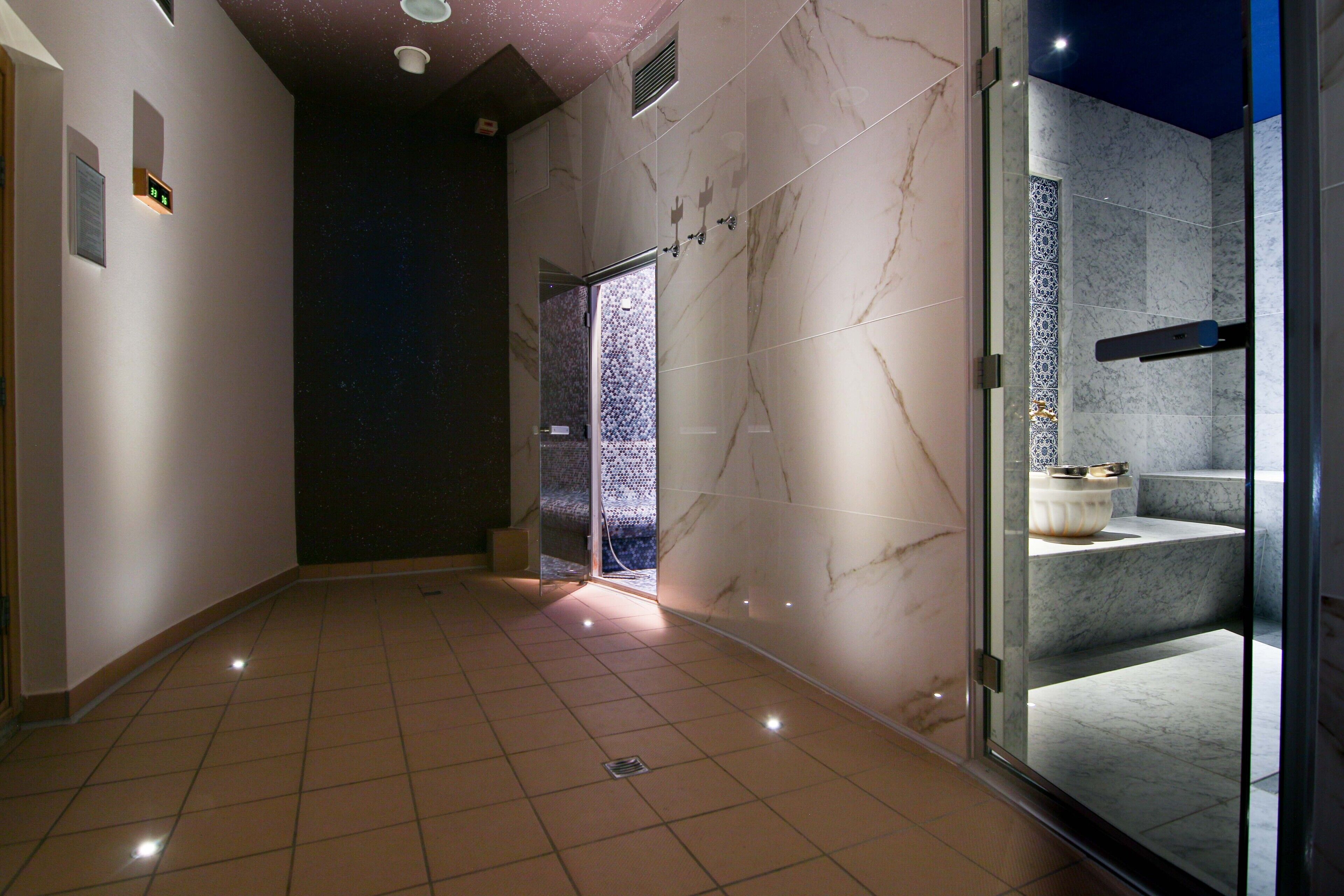 A modern bathroom with a glass shower enclosure, marble walls, and a tiled floor.