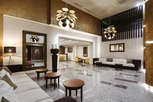 A spacious lobby with a modern design, featuring a large sofa, a coffee table, and a seating area with chairs.