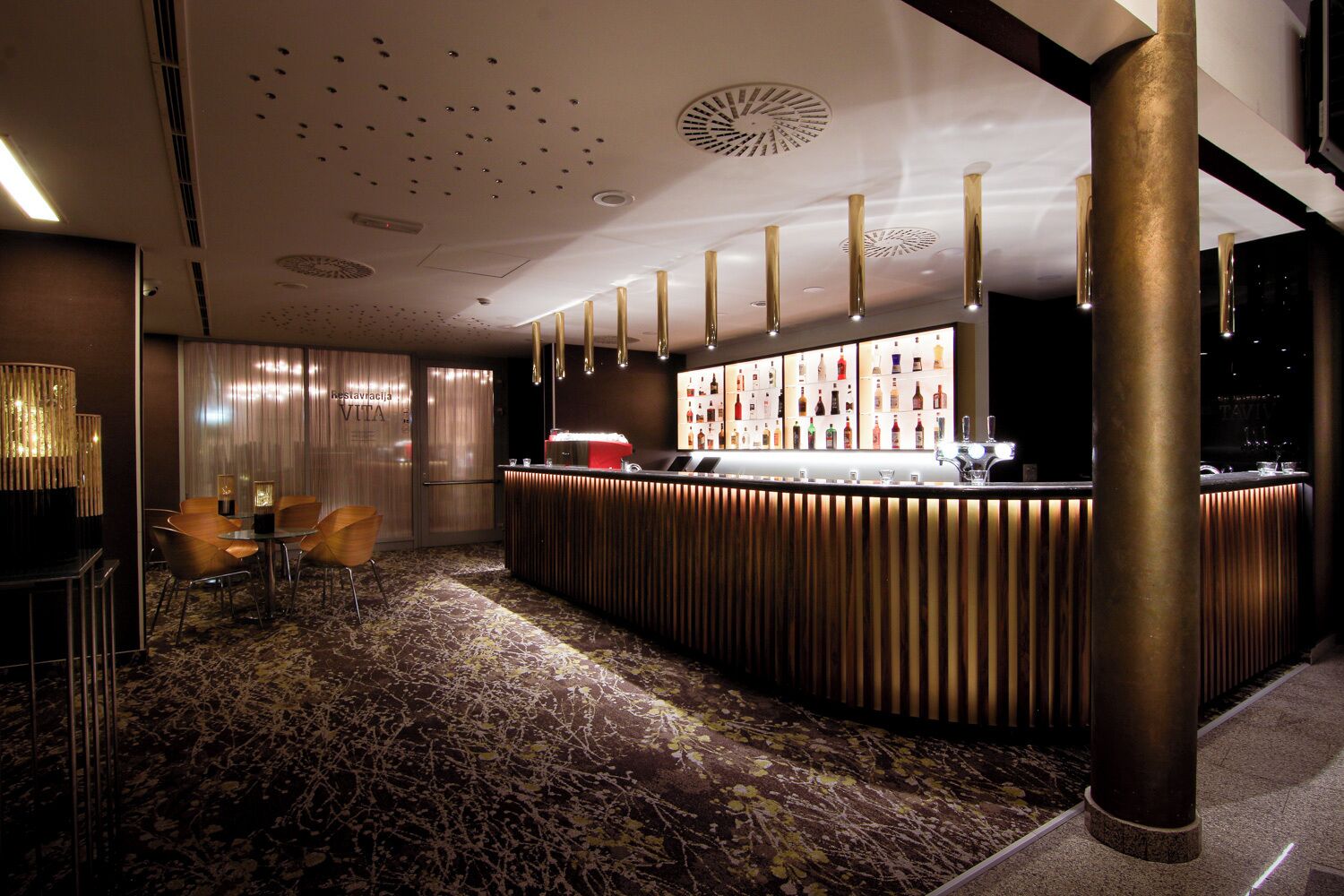 Een bar met een houten toonbank, barkrukken en een assortiment flessen.