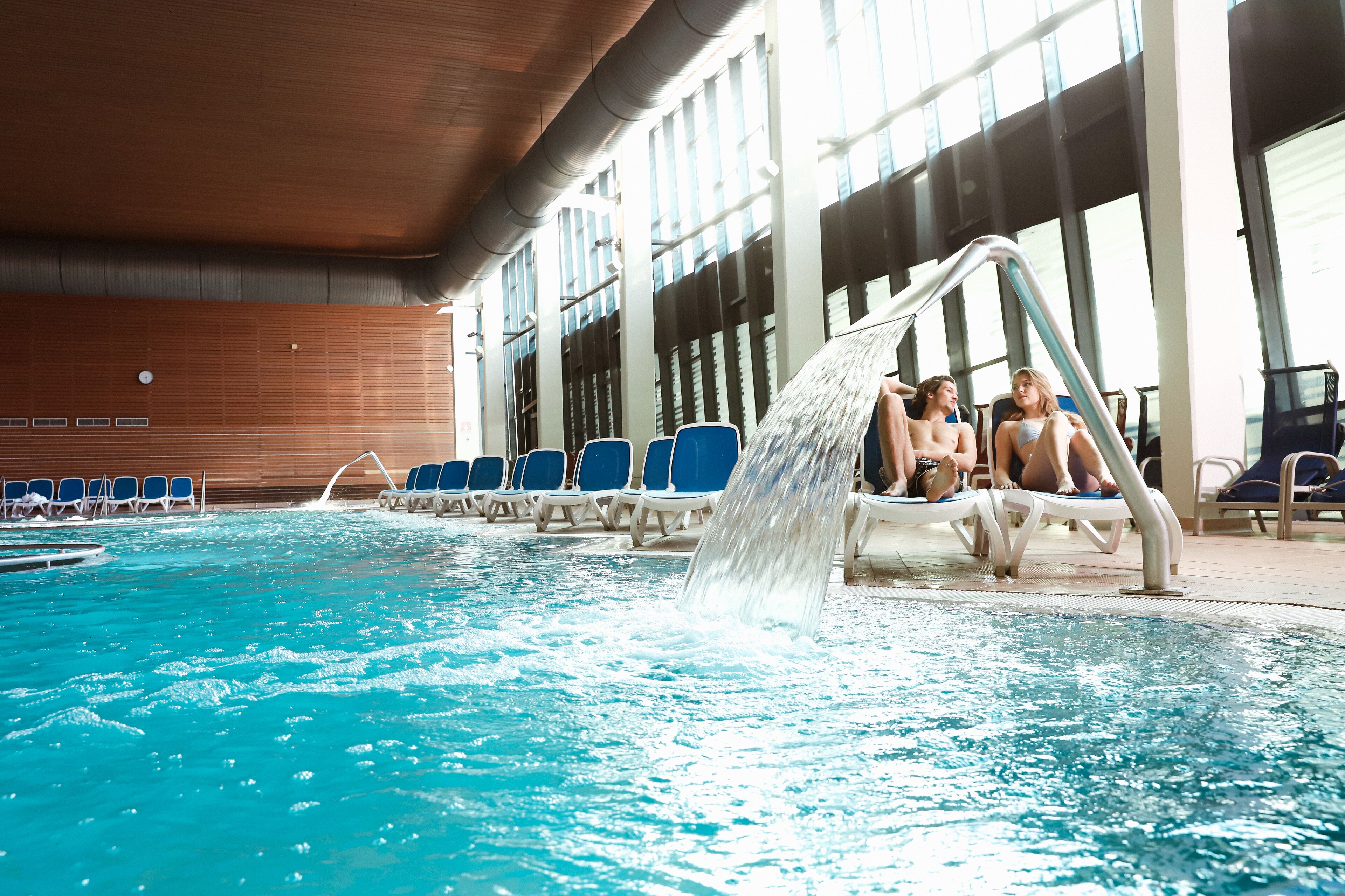 Une piscine intérieure à l’eau d’un bleu limpide, avec des chaises bleues et un élément décoratif aquatique.
