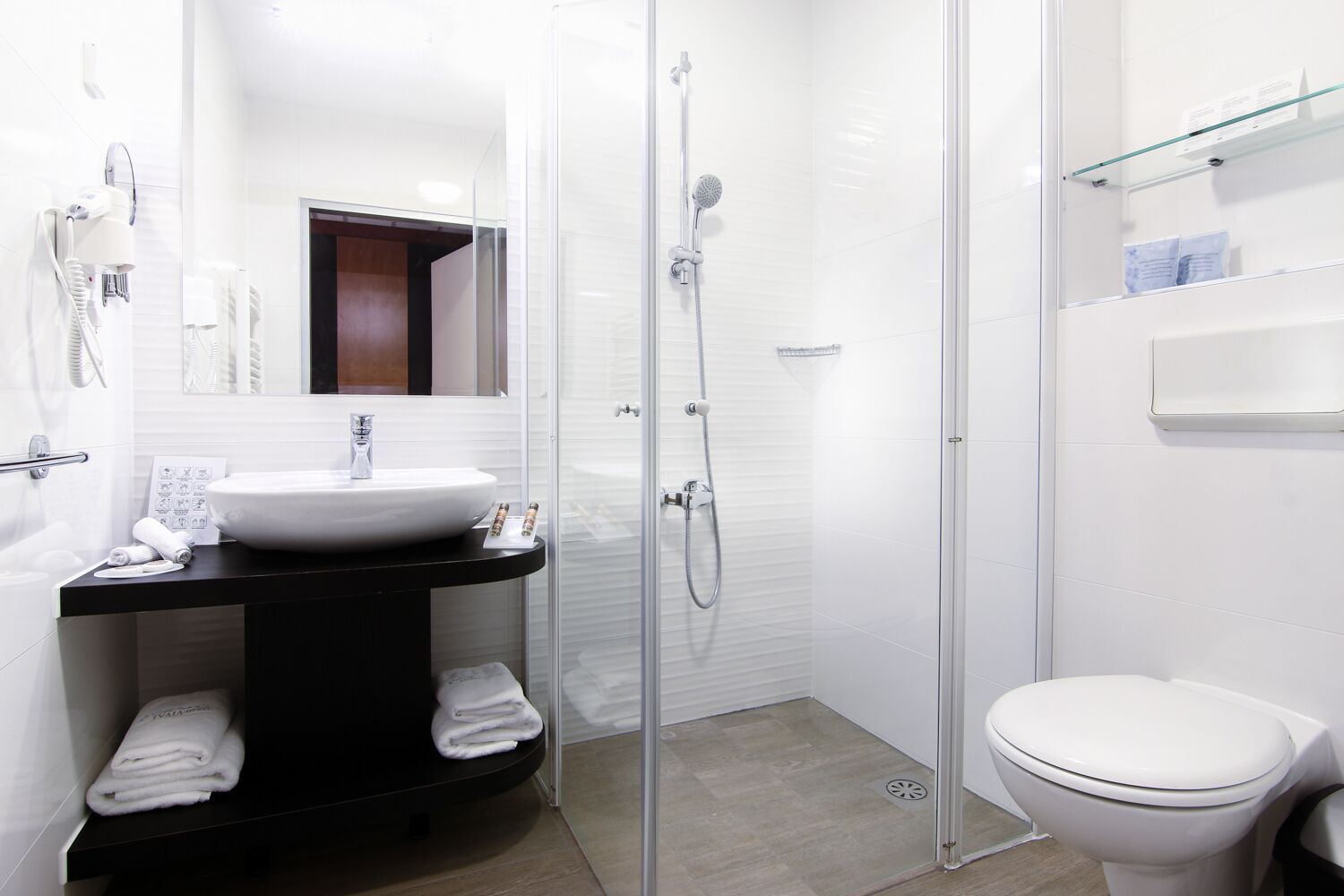 Un baño moderno con ducha envuelta en vidrio, lavamanos blanco y retrete.