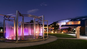 Um edifício moderno com fachada de vidro e um espelho d'água circular com iluminação roxa.