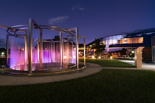 A modern building with a glass facade and a circular water feature with purple lighting.
