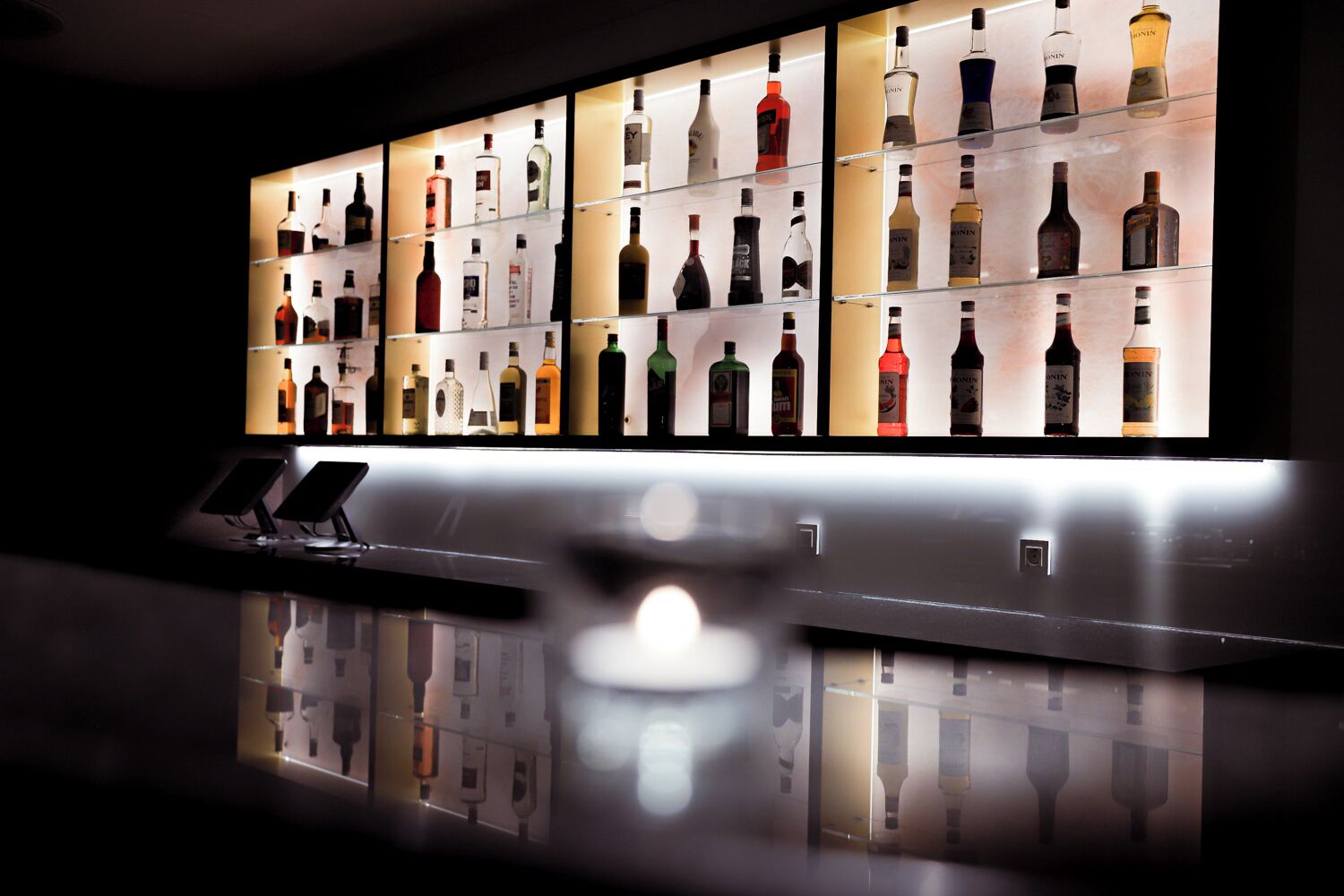 A bar area with multiple shelves displaying various bottles of alcohol.