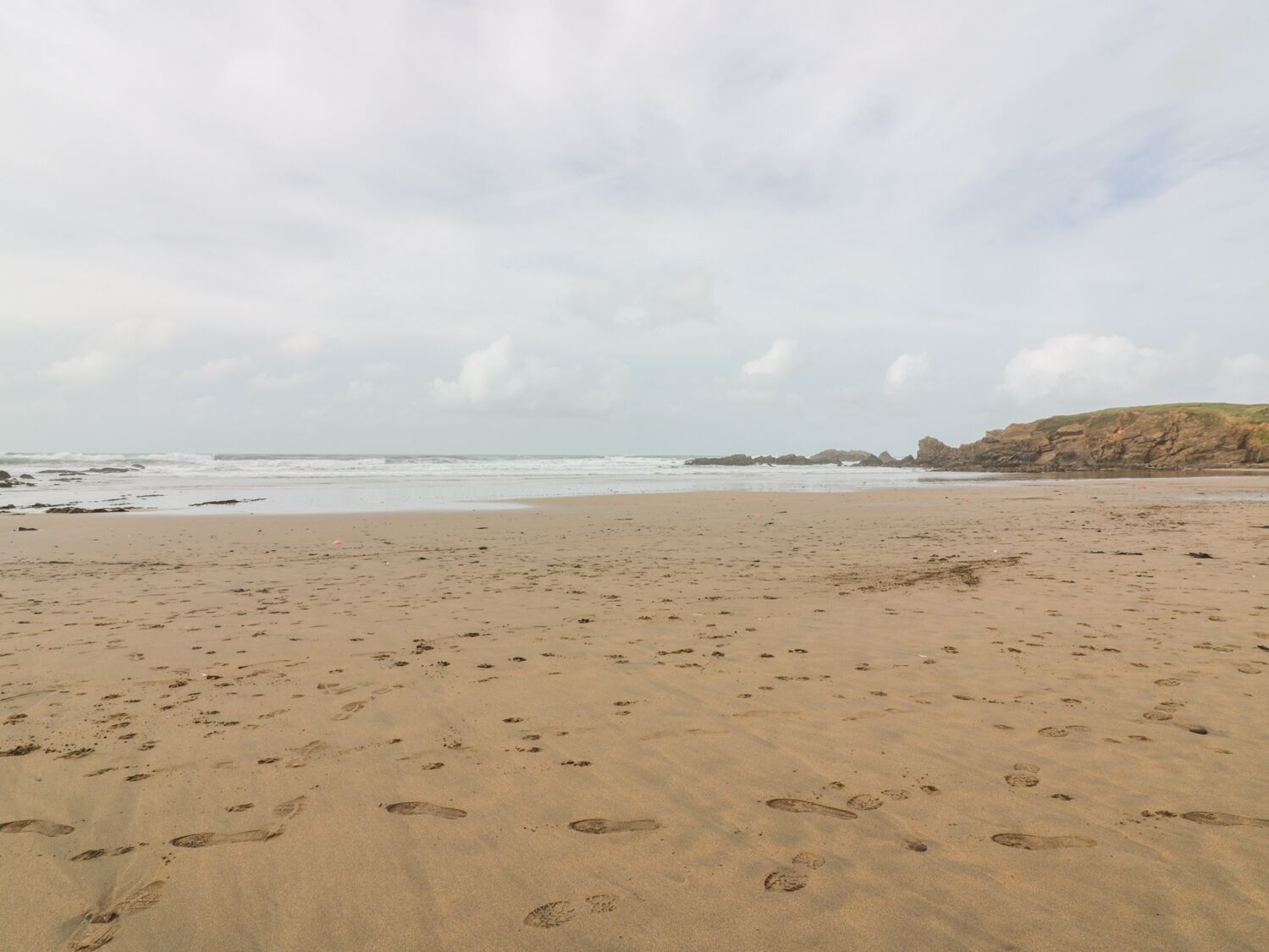 A beach with footprints in the sand and rocky cliffs in the background.