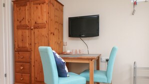 Una habitación con un armario de madera, un televisor fijado a la pared, una mesita de madera, dos sillas turquesas y un radiador.