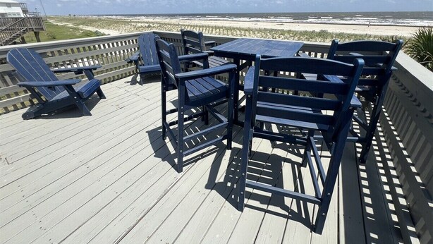 A wooden deck with blue chairs and a table overlooking a beach.