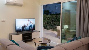A living room with a TV, sofa, and a glass door leading to an outdoor area. -  Bay View Gardens Apts with Pool by TrulyCyprus (Limassol)