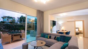 A modern living room with a sofa, coffee table, and dining area. -  Bay View Gardens Apts with Pool by TrulyCyprus (Limassol)