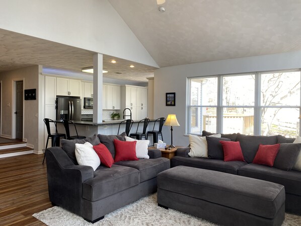 A modern living room with a grey sectional sofa, a white rug, and a dining area with black chairs.