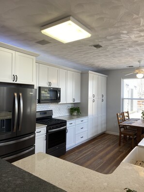 A modern kitchen with white cabinetry, stainless steel appliances, and a wooden dining table.