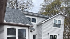 Una terraza con mobiliario exterior, un porche cubierto y una casa de fachada gris y detalles blancos.