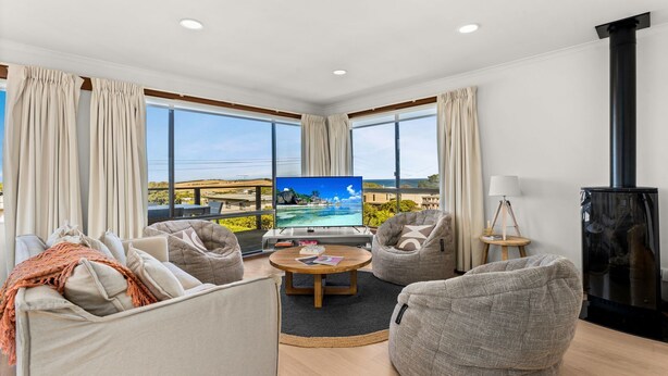 Ett modernt vardagsrum med en stor TV, bekväma sittplatser och utsikt över havet.