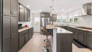 A modern kitchen with dark cabinets, a central island, stainless steel appliances, and pendant lighting.