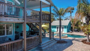 A two-story building with a balcony, a pool, and a small house in the background.