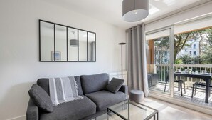 Ett modernt vardagsrum med en grå soffa, ett soffbord i glas och ett stort fönster med utsikt över omgivningen.