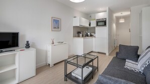Ett modernt vardagsrum med ett soffbord i glas, en grå soffa och en platt-TV placerad på ett vitt skåp.