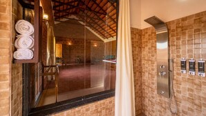 A modern bathroom with a glass shower enclosure, a towel rack with rolled towels, and a wall-mounted showerhead. - Gudlu (Mudigere)