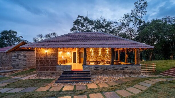 A stone building with a tiled roof, a wooden deck, and a stone pathway leading to the entrance. - Gudlu (Mudigere)