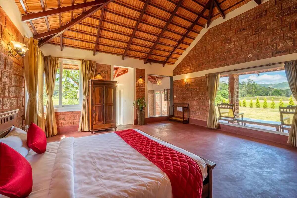 A spacious bedroom with a large bed, a wooden wardrobe, and a view of the garden through a large window.
