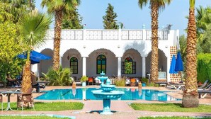 A pool area with a fountain, palm trees, and a building with arched windows. - Serene haven on the outskirts of Marrakech w/ pool (Marrakech)