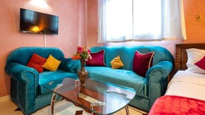 A room with two teal sofas, a glass coffee table, a flat-screen TV mounted on the wall, and a bed with a red blanket. - Serene haven on the outskirts of Marrakech w/ pool (Marrakech)