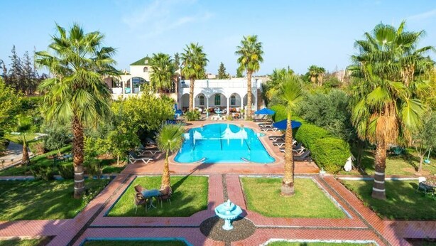 A pool area with palm trees, a fountain, and a building with arches in the background. - Serene haven on the outskirts of Marrakech w/ pool (Marrakech)