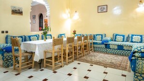 A dining area with a white table, blue patterned sofa, and wooden chairs. - Serene haven on the outskirts of Marrakech w/ pool (Marrakech)