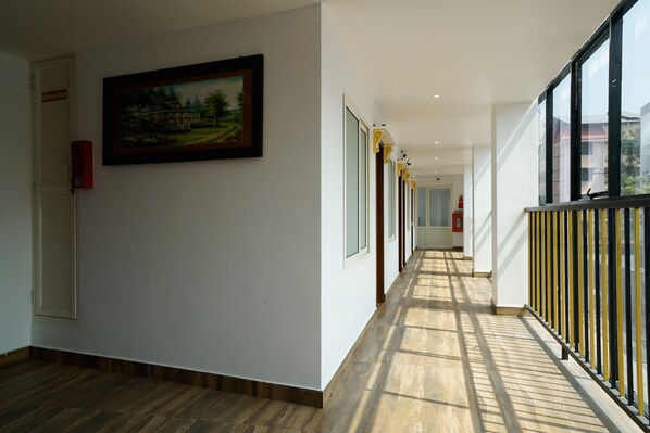 A long, narrow hallway with wooden flooring, white walls, and large windows on one side.