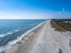 Ein Strand mit einer weiten Sandfläche, einige Personen, die spazieren gehen, und Gebäuden im Hintergrund.