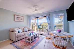 Relax in this inviting living room with a sofa, coffee table, and flat-screen TV, surrounded by large windows offering a view of the outdoors.