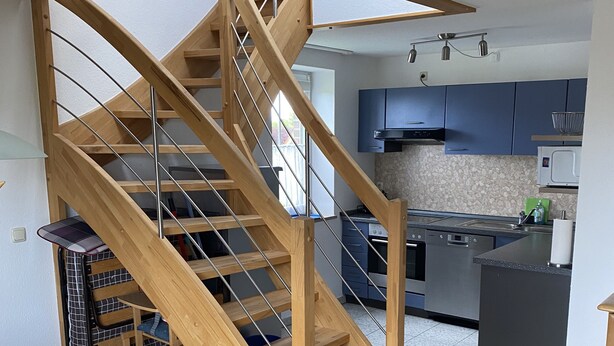 Una cocina moderna con armarios oscuros, una escalera de madera y un comedor con mesa y sillas.